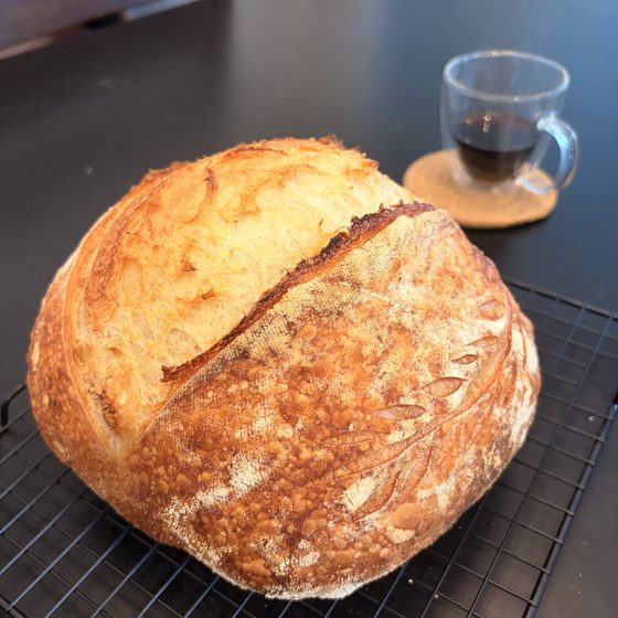 A round golden sourdough loaf cooling on a wire rack.