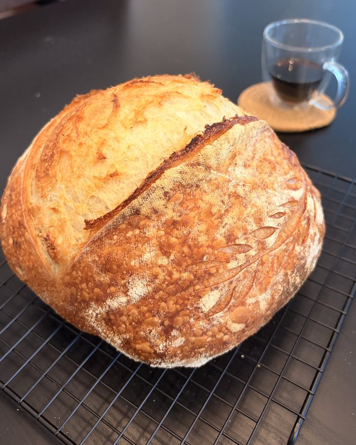 A round sourdough boule cooling on a wire rack, crust deep gold and split along a single curved score.