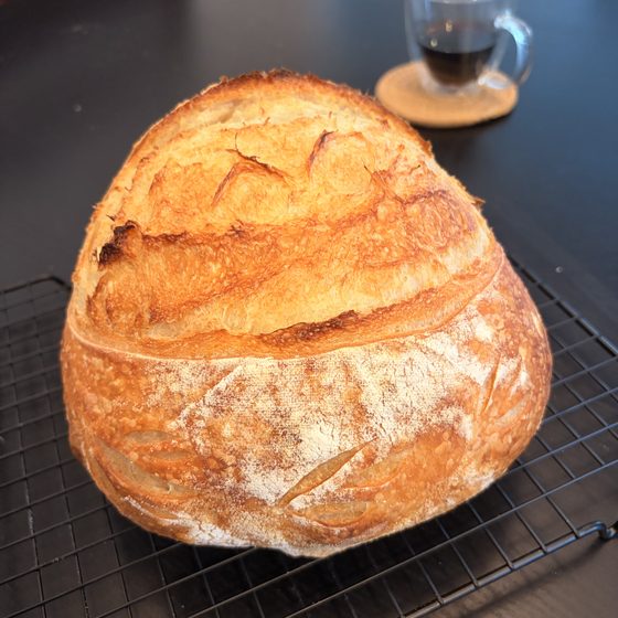 A round sourdough loaf with a curved score, cooling on a wire rack.
