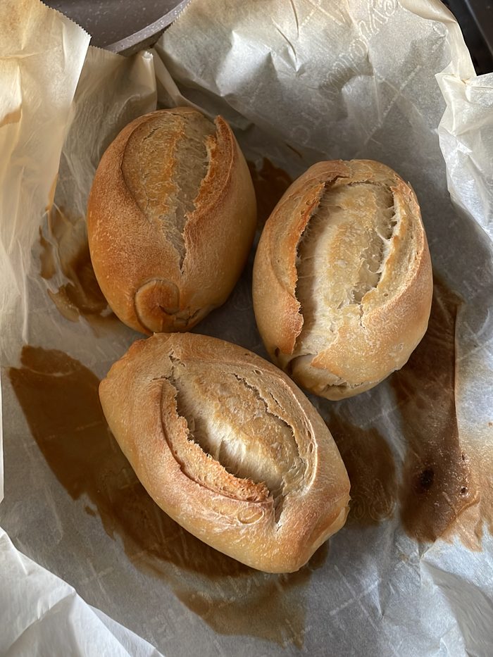 Three golden pão francês rolls with a deep centre slash, fresh from the oven.