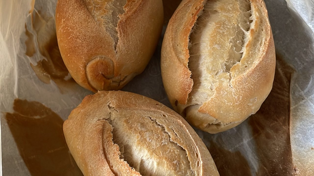 Three baked pão francês rolls resting on parchment paper, crusts split and golden.