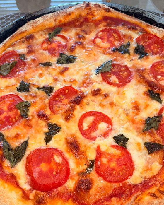 A margherita pizza baked on a hot pan, with blistered mozzarella, tomato slices and basil.