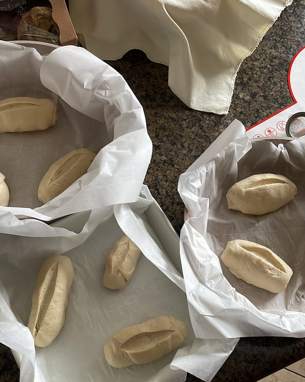 Trays of pale shaped dough rolls resting on parchment paper before baking.