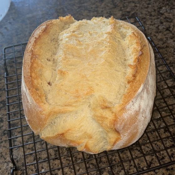 A round golden sourdough loaf cooling on a wire rack.